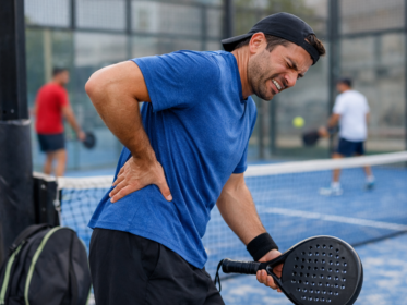 Giocatore principiante di padel con mano sulla zona lombare dopo uno scambio, campo da padel sullo sfondo